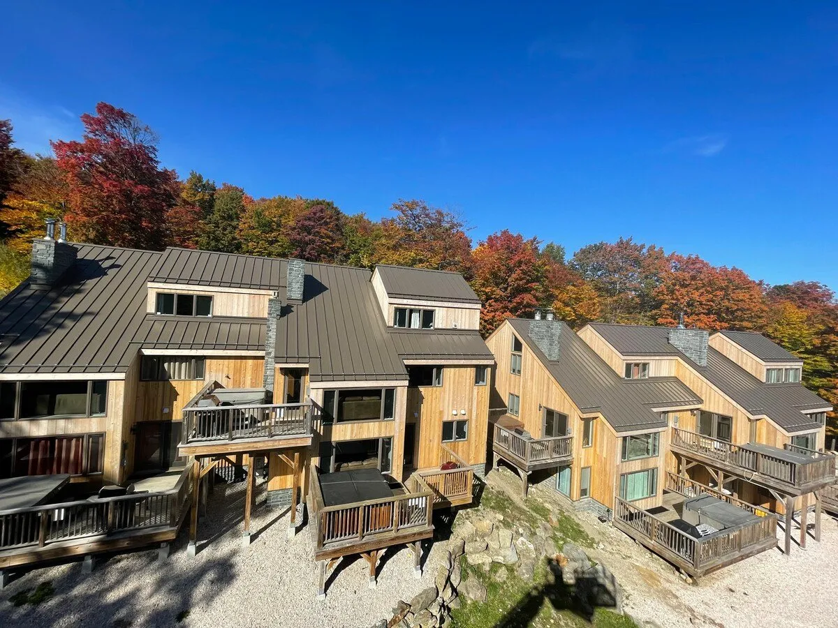 The photo showcases several wooden cabins with balconies overlooking a landscape awash in autumn foliage. The atmosphere is cozy and serene, with hints of social gatherings on the balconies or around a fire pit.