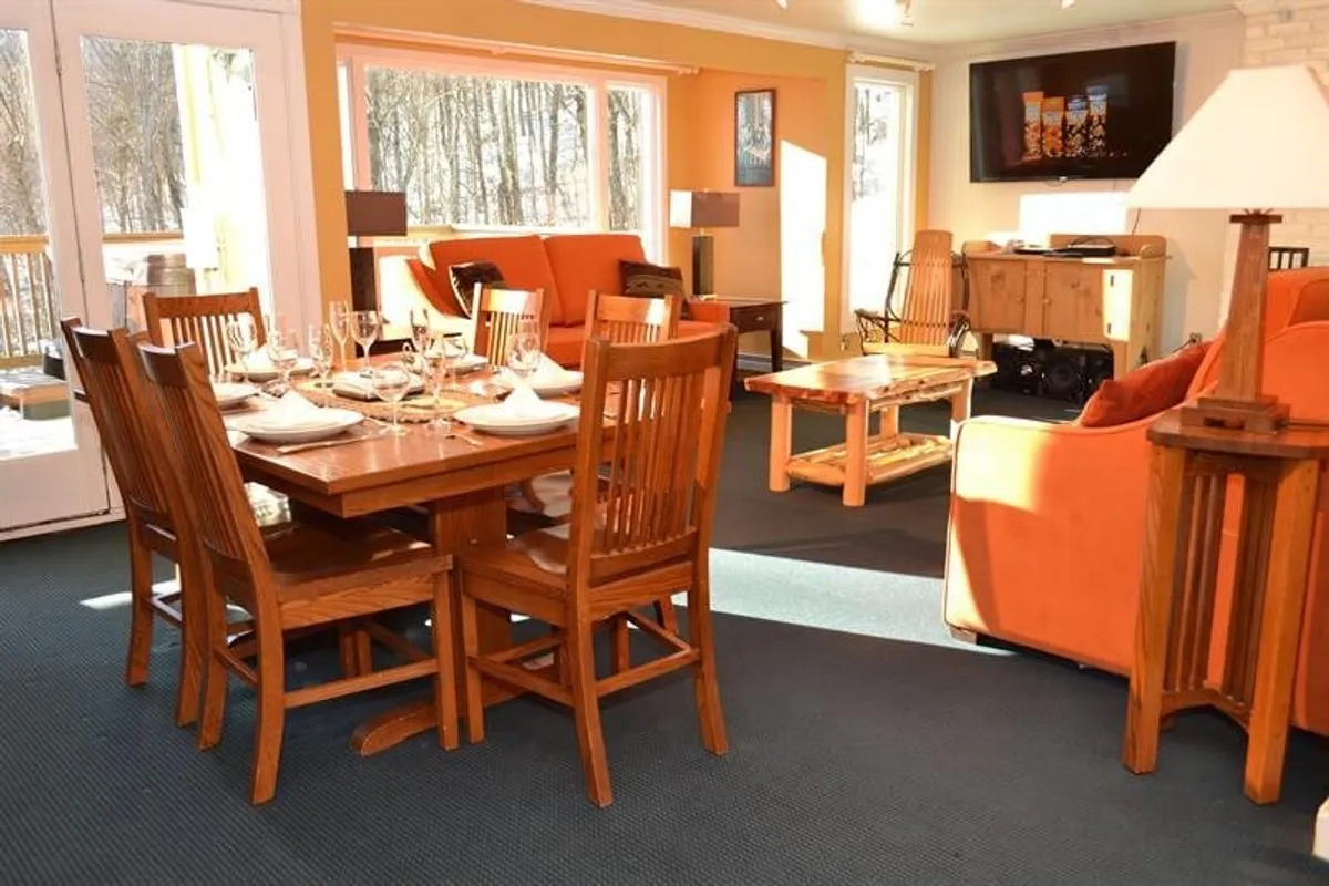 A dining table is beautifully set for a meal, surrounded by comfortable orange sofas and flooded with natural light from large windows. The atmosphere is warm and welcoming, perfect for family gatherings or intimate dinners.