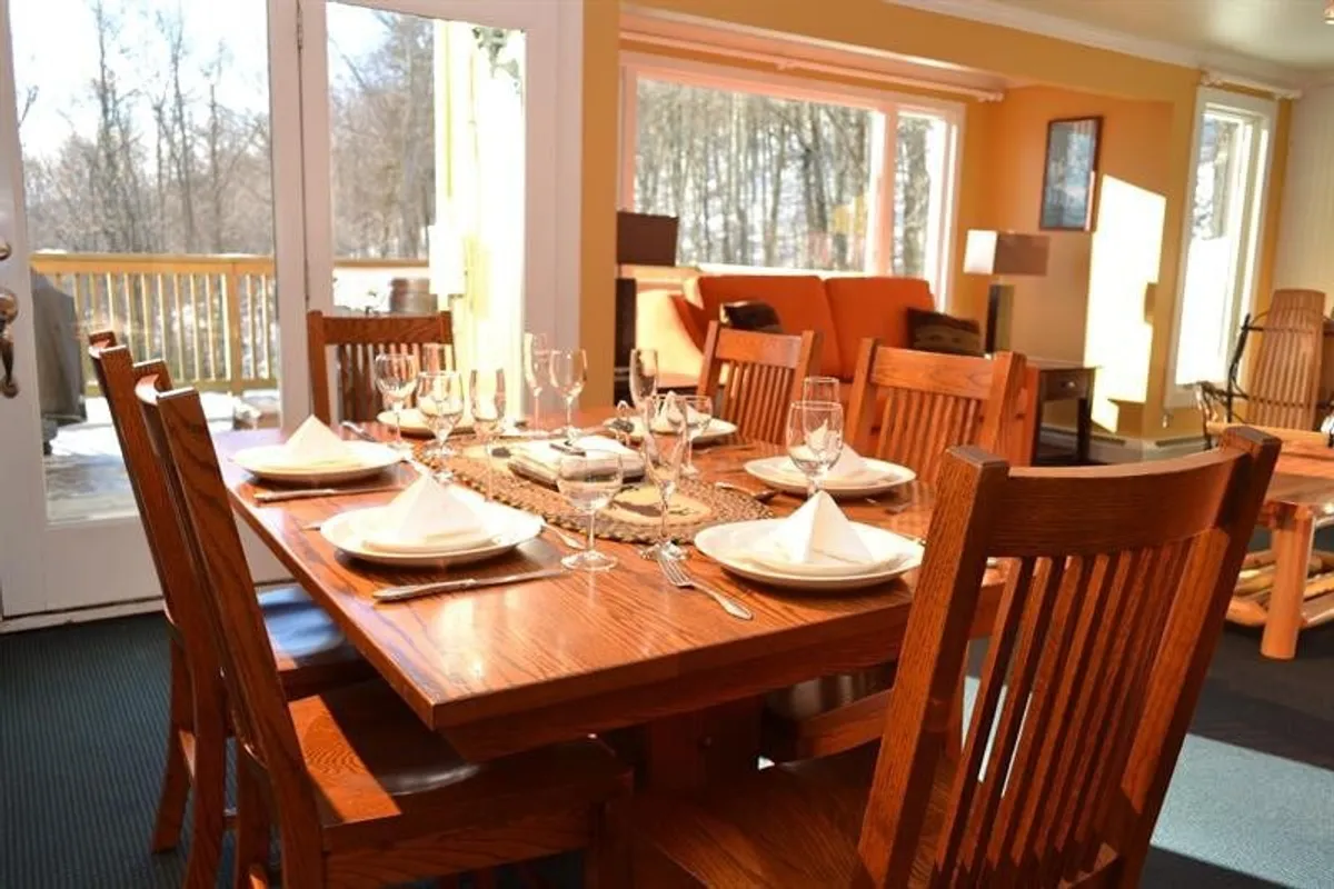 The dining table, beautifully set for a meal, sits beside large windows that flood the space with natural light. The ambiance speaks to shared meals and joyful moments, with views that hint at the scenic outdoors.