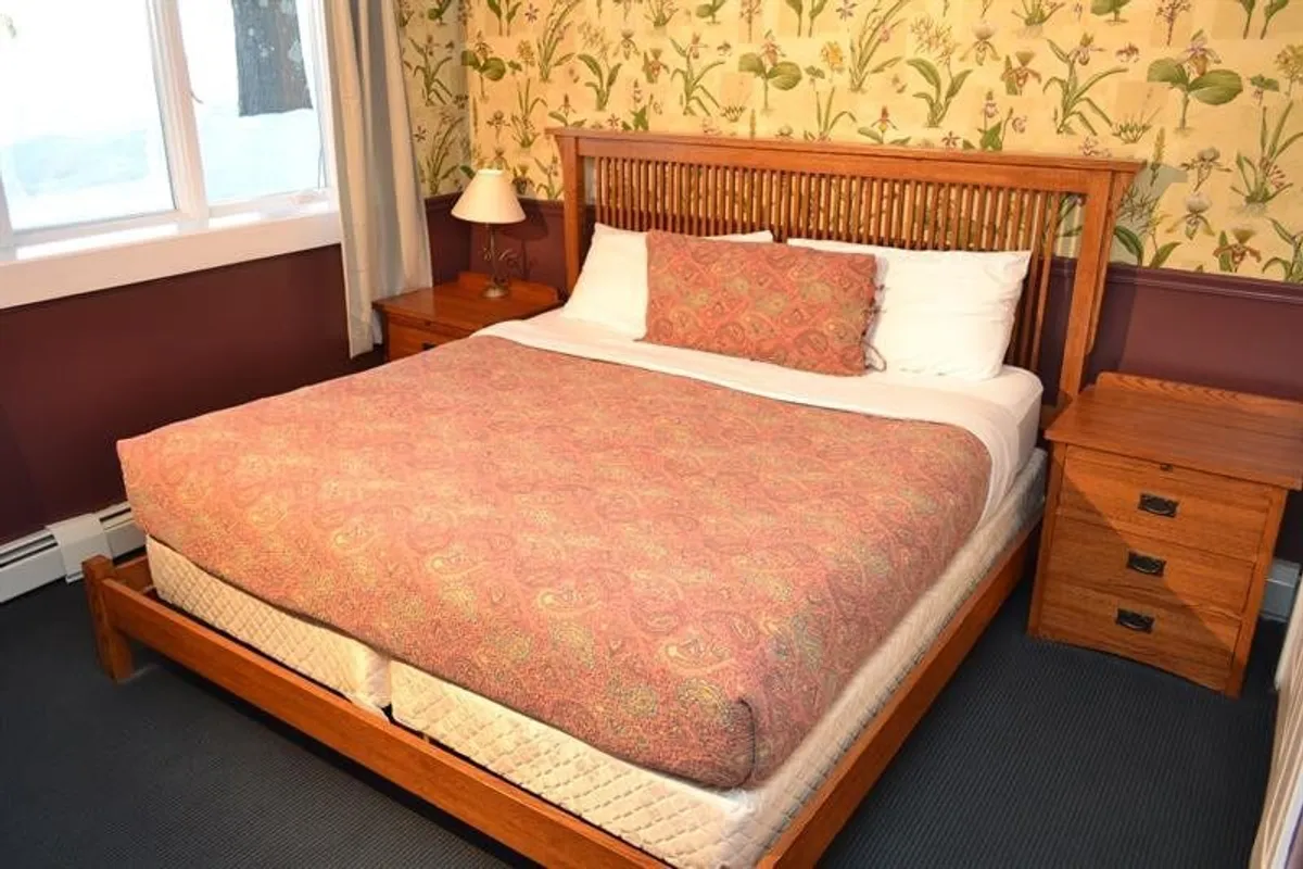 The image shows a cozy bedroom with a king-size bed as the focal point, accented by floral wallpaper and flanked by inviting nightstands. Soft lighting and subtle decor create a restful and welcoming atmosphere, perfect for unwinding after a day of adventure or for couples seeking a private retreat.