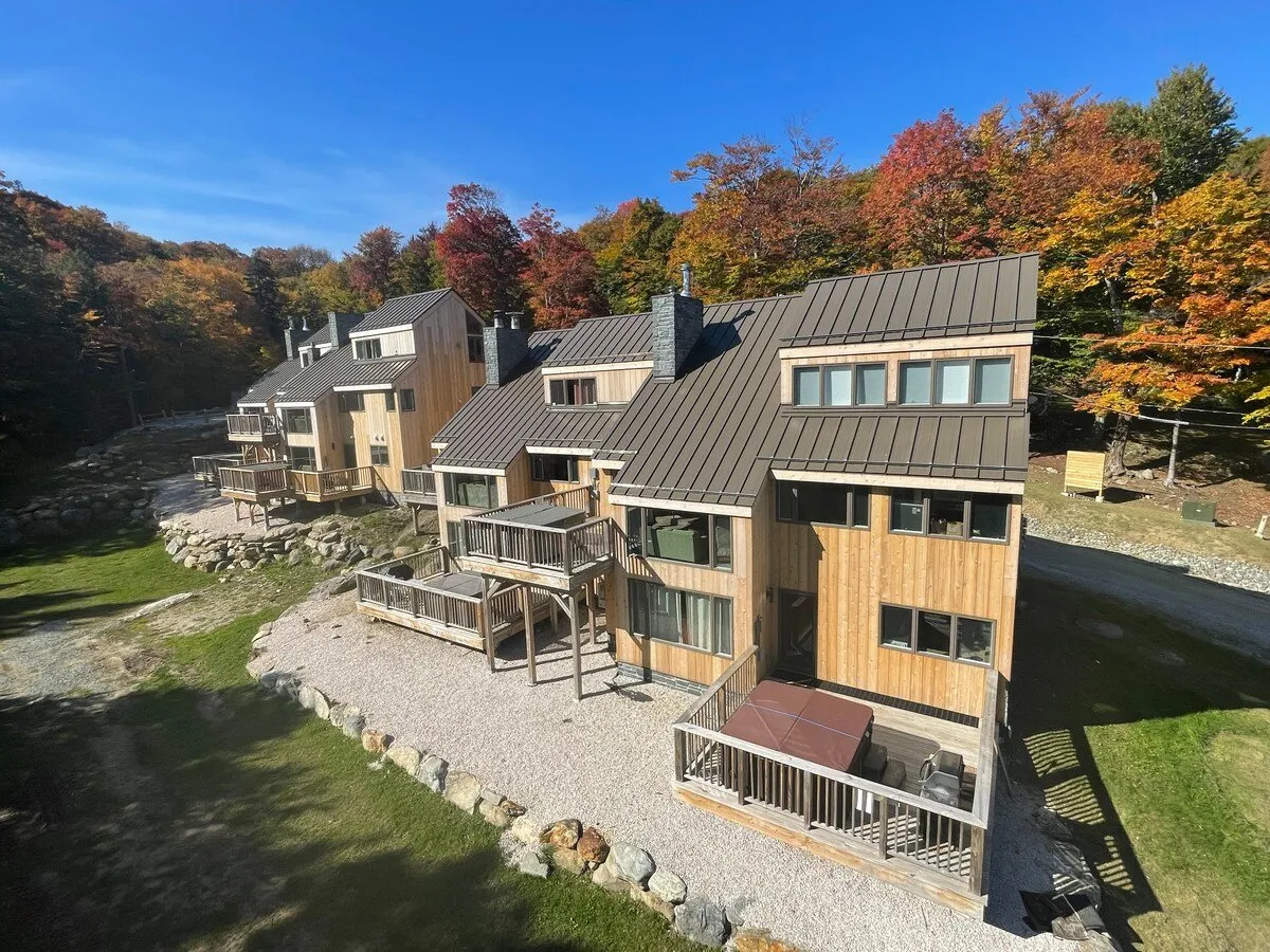 A serene exterior view showcasing modern wooden cabins, colorful autumn foliage, and spacious outdoor decks. The decks are well-suited for relaxing or gathering with friends and family, with an inviting atmosphere for barbecues or morning coffee outdoors.